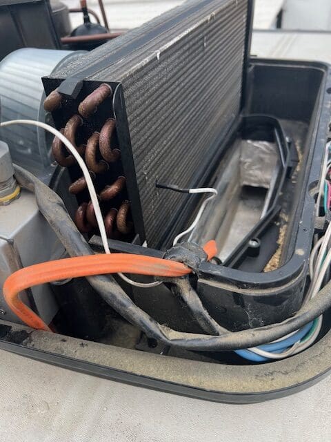 A broken air conditioner unit with wires and cords.