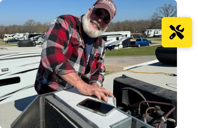 A man in plaid shirt and hat standing next to an air conditioner.